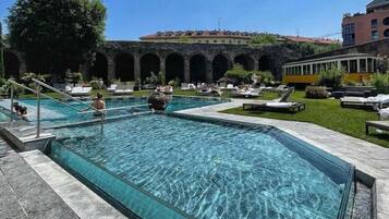 A swimming pool with clear water, surrounded by lounge chairs and a building with arches in the background.