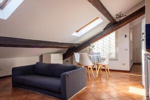 Um quarto estilo loft com teto inclinado, um sofá, uma mesa de jantar com cadeiras e uma janela.