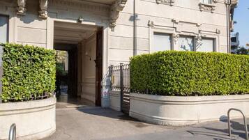 A building entrance with a gated driveway, a clear pathway, and a hedge.