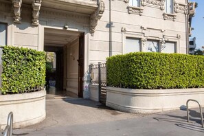 Entrada de um edifício com portão na entrada, caminho acessível e cerca viva.