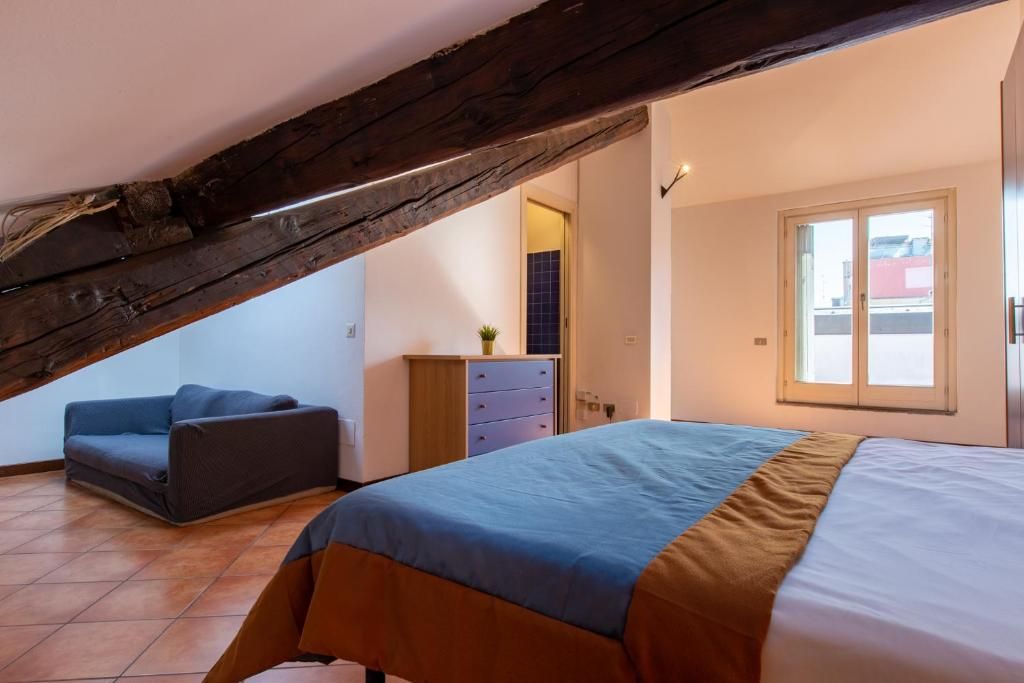 Un dormitorio con techo inclinado, una cama con cubrecama azul y marrón, un sofá azul y un aparador de madera.