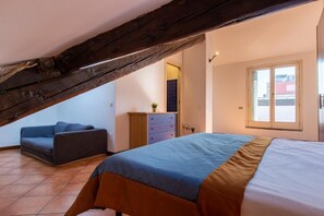 Quarto com teto inclinado, cama com colcha azul e castanha, sofá azul e cómoda de madeira.
