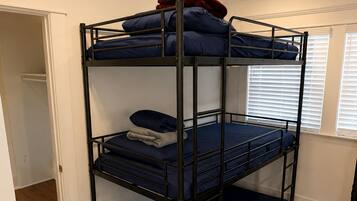 Ein Etagenbett mit drei Schlafstellen, Holzboden und ein Fenster mit Jalousien.