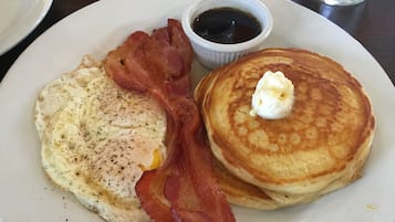 A plate with a fried egg, bacon, and pancakes with butter.