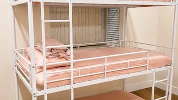 A bunk bed with three levels, each with a mattress and pillows, in a room with wooden flooring and a window with blinds.