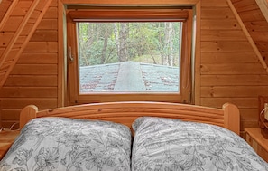 Ein Zimmer in einer Holzhütte mit einem Bett und einem Fenster mit Blick auf einen Waldweg.