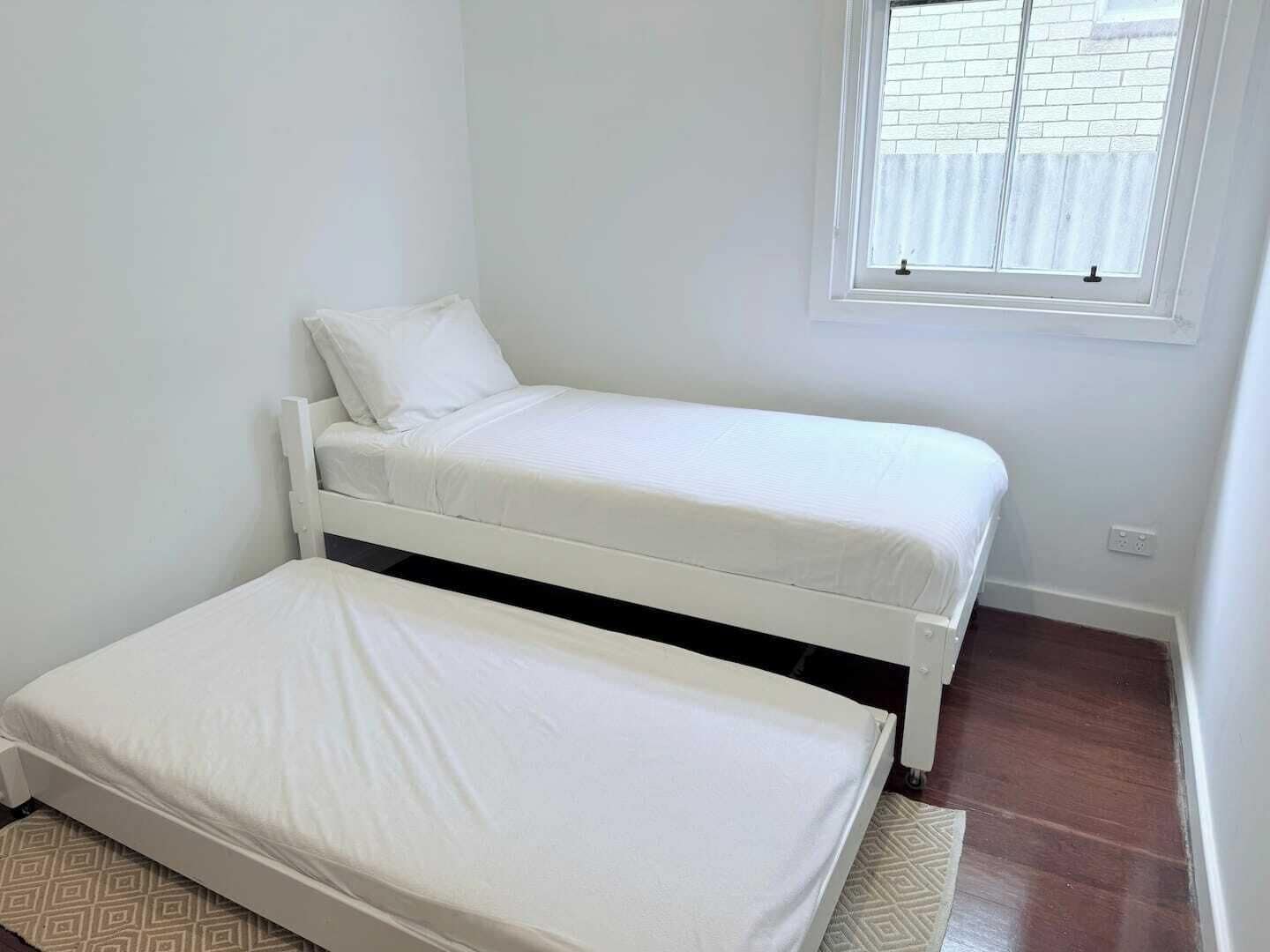 Ein kleines Zimmer mit einem Einzelbett, einem Fenster und einer Tür.