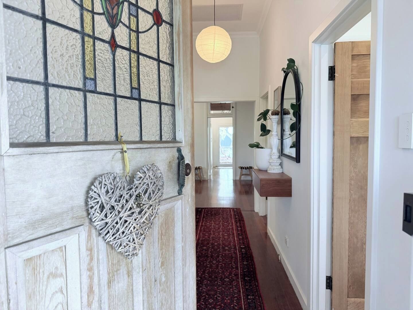 A hallway with a wooden door, a red patterned rug, and a hanging light fixture.
