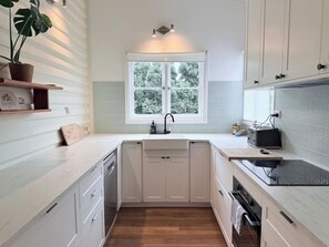 A modern kitchen with white cabinetry, a wooden countertop, a window with a view of greenery, and a built-in dishwasher. - Harvey’s Beach House Close to South Beach (South Fremantle)