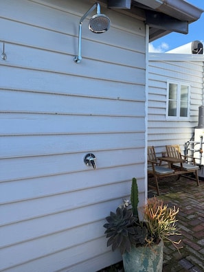 A house with a metal showerhead mounted on the exterior wall, a door handle, and a potted plant with a cactus and other foliage. - South Beach Hideaway Studio- Close to Beach (South Fremantle)