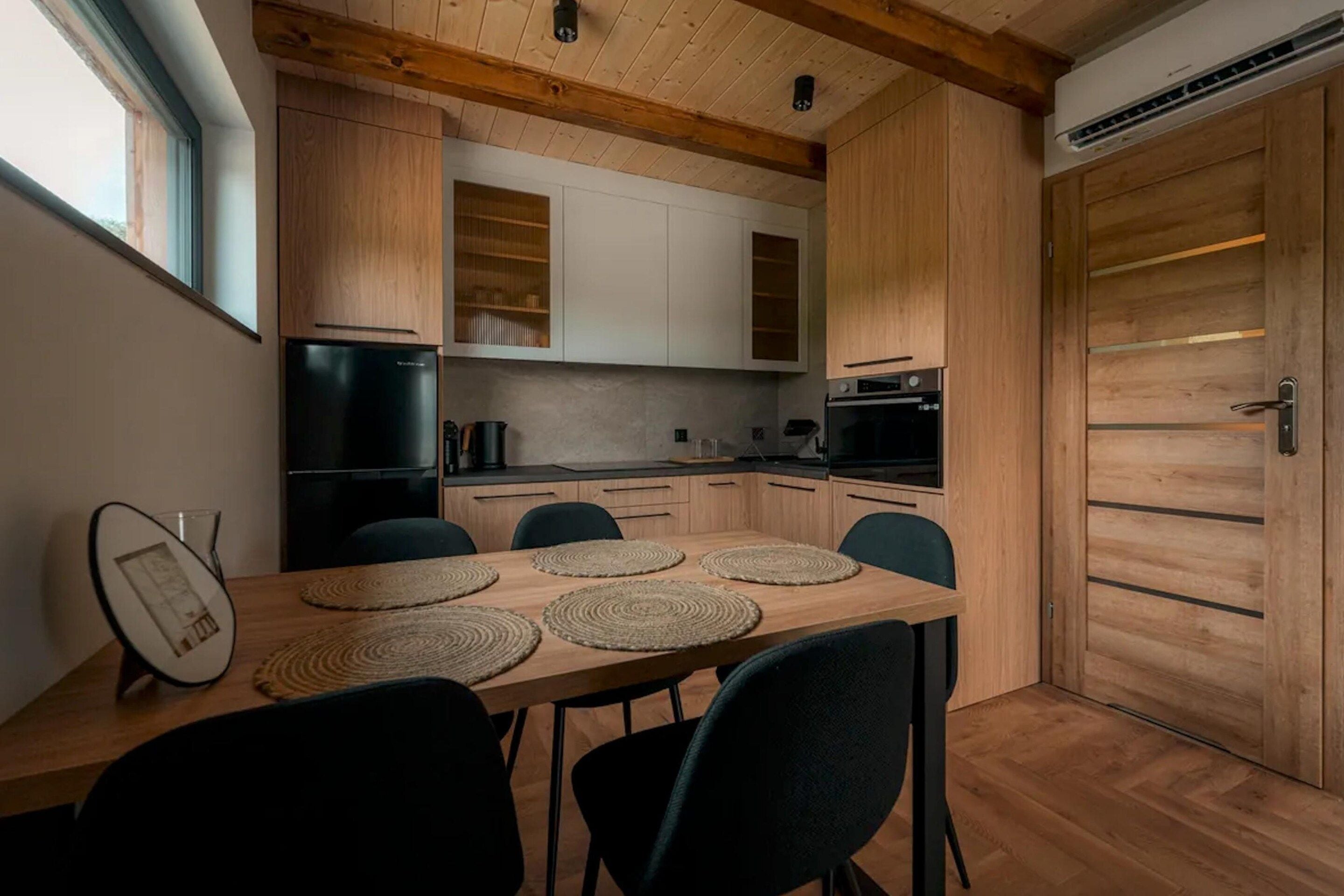 A modern kitchen with wooden cabinets, a dining table with placemats, and a large wooden door.