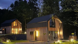 Una cabaña moderna de madera con techo inclinado, ventanas amplias y una entrada bien iluminada.