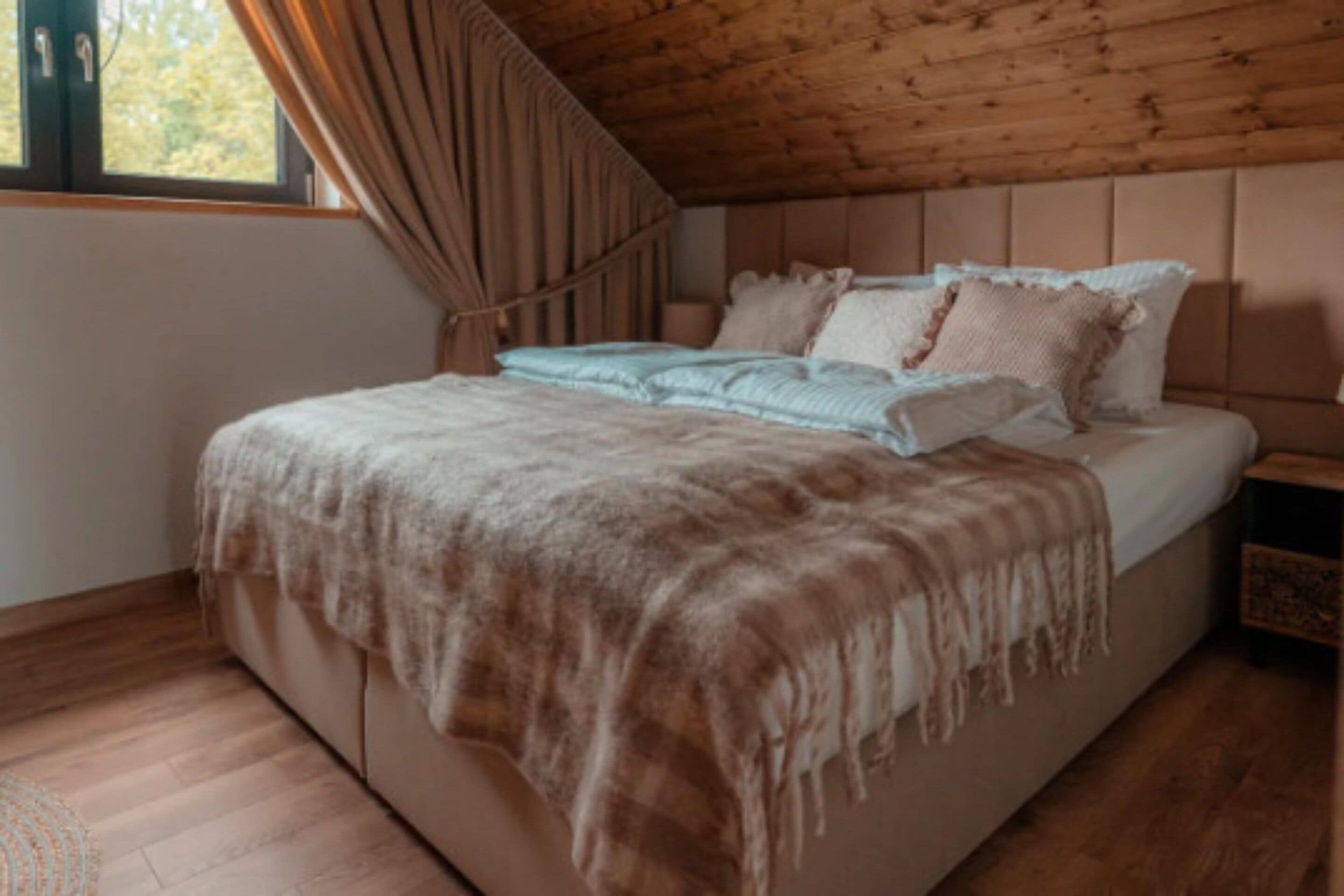 A bedroom with a wooden ceiling, a bed with a white and brown blanket, and a nightstand with a lamp.