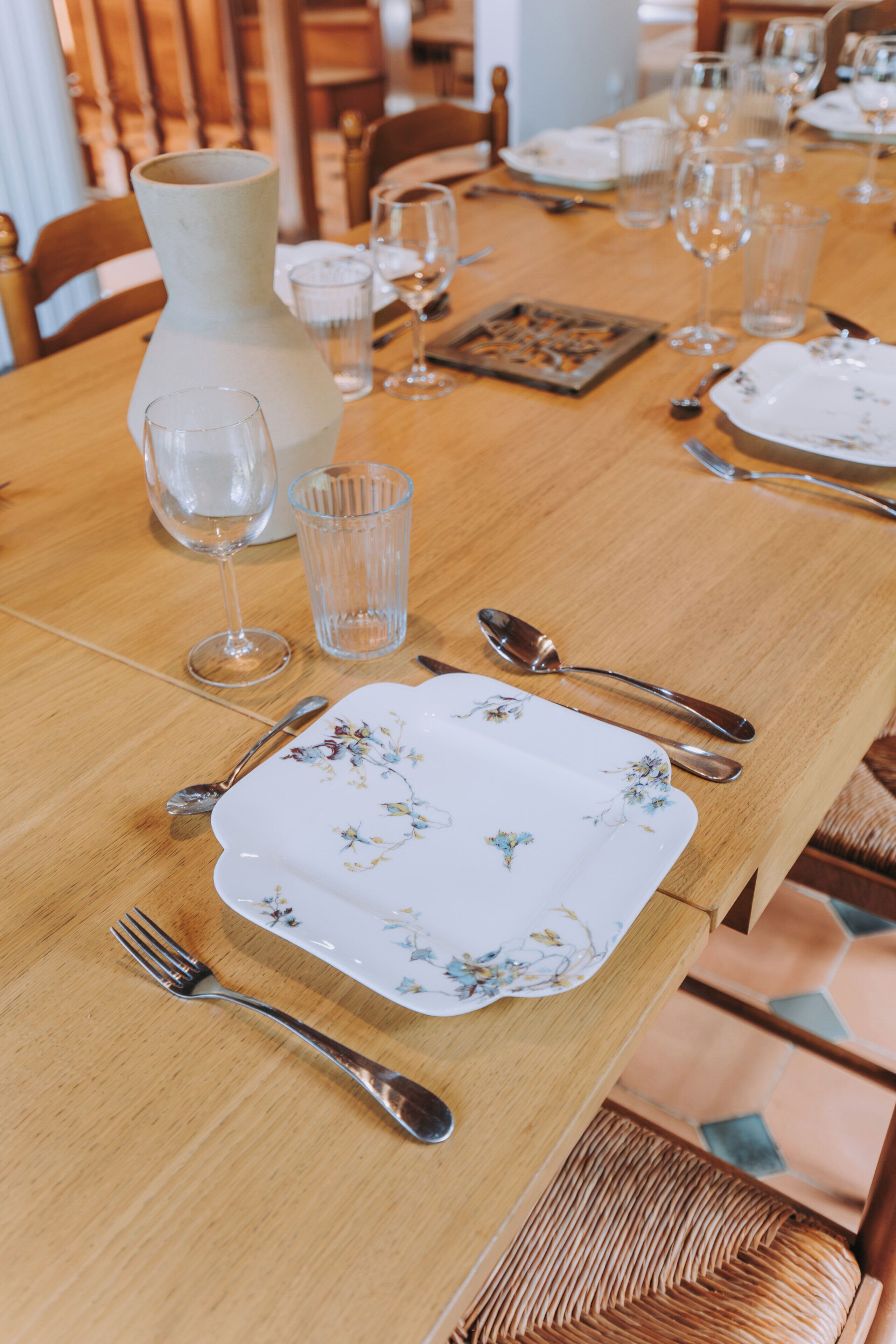 Une table à manger dressée avec des assiettes, des couverts, des verres et un vase.