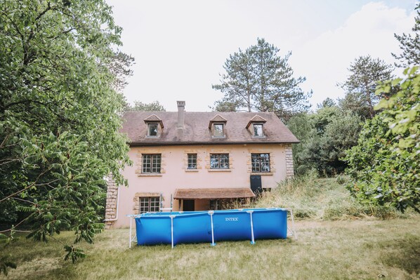 A two-story house with a sloped roof, multiple windows, and a chimney. In front of the house, there is a blue dumpster.