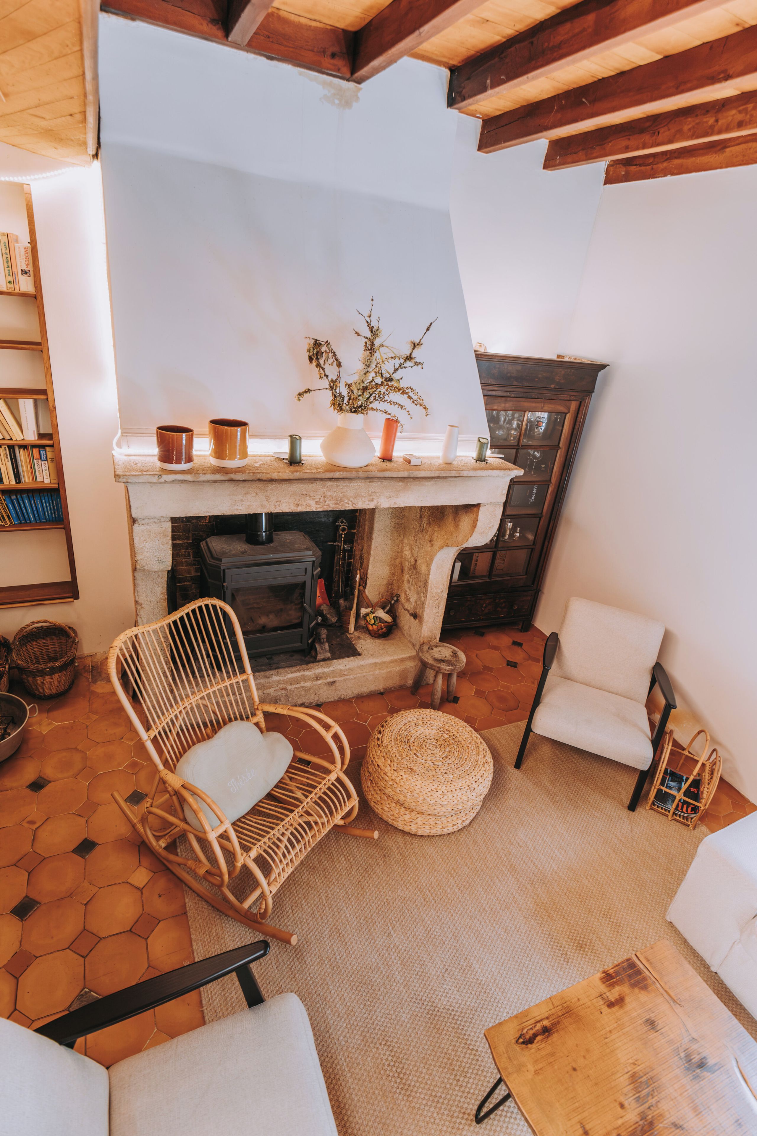 A cozy living room with a fireplace, wicker furniture, and a bookshelf.