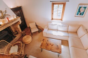 A cozy living room with a fireplace, a sofa, a coffee table, and a wicker chair.