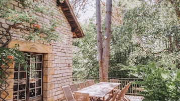 Un bâtiment en pierre avec une table et des chaises en bois, entouré de verdure et d’arbres.