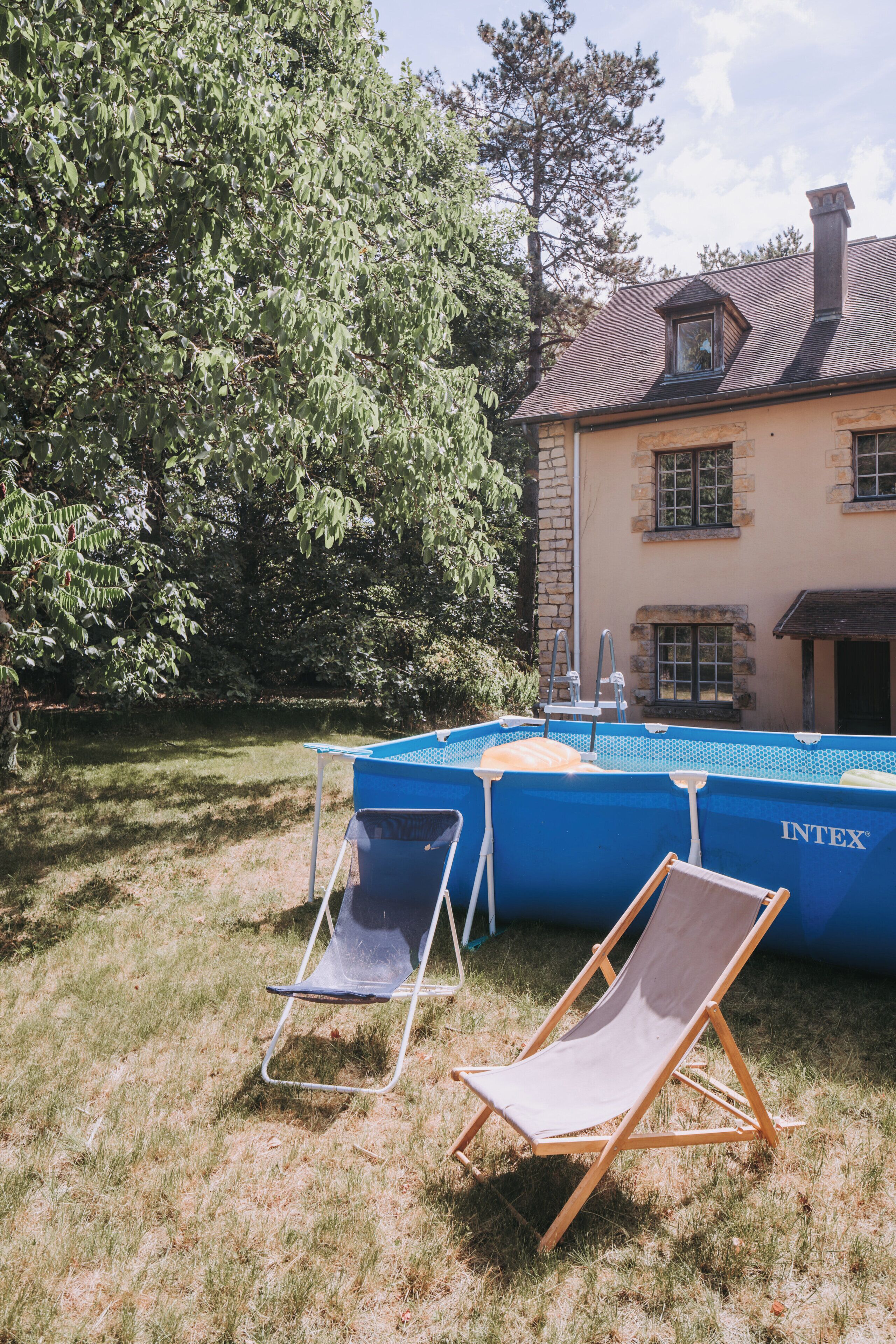 A swimming pool with a ladder, two lounge chairs, and a house in the background.