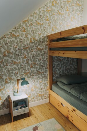 A room with a bunk bed, a small bedside table with a lamp, and a bookshelf.