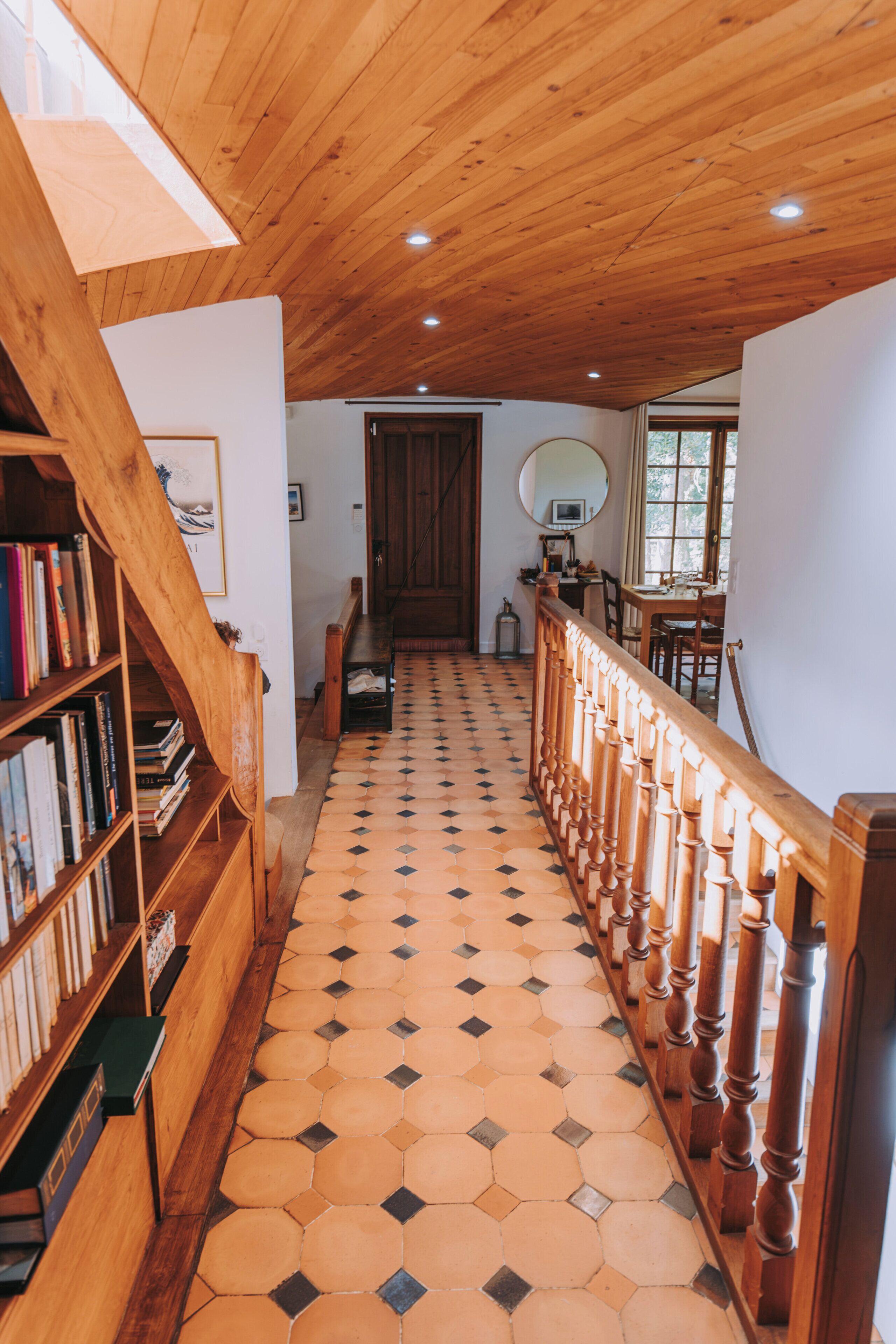 Un pasillo con una escalera de madera, una estantería y una zona de comedor con una mesa y sillas.