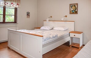 Ein Schlafzimmer mit einem weißen Bett, einem Holzkopfende, Nachttischen und einem Fenster mit Vorhängen.