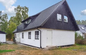 Ein eingeschossiges Haus mit dunklem Dach und weißen Wänden, einer Haustür und einer kleinen Veranda mit einem Stuhl.