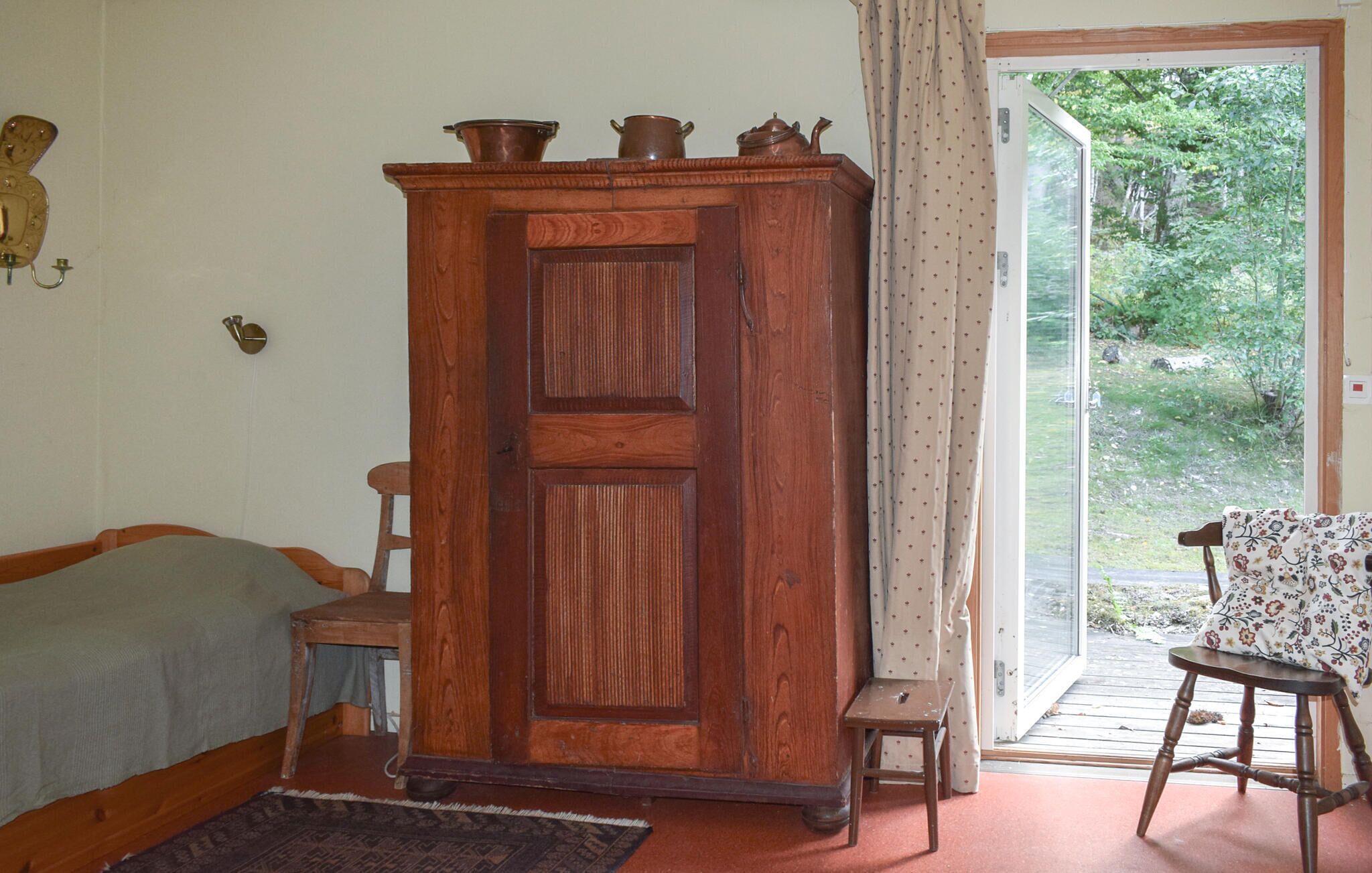 Une pièce comprenant une armoire en bois, un lit, une chaise, une petite table et une porte donnant sur un espace extérieur.