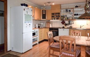 A kitchen with a white refrigerator, stove, microwave, wooden chairs, and a dining table. - 3 bedroom stunning home in Backaryd (Backaryd)