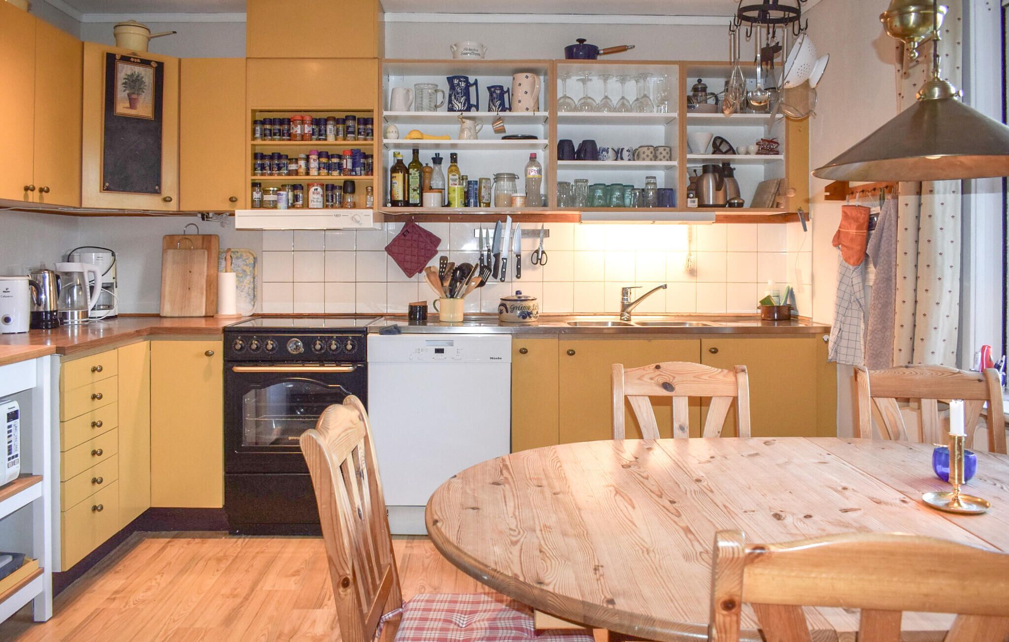 Una cocina con armarios de madera, estufa, lavavajillas y una mesa de comedor con sillas.