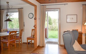 A dining area with wooden chairs and a table, a living room with a sofa, a clock on the wall, and a door leading outside. - 3 bedroom stunning home in Backaryd (Backaryd)