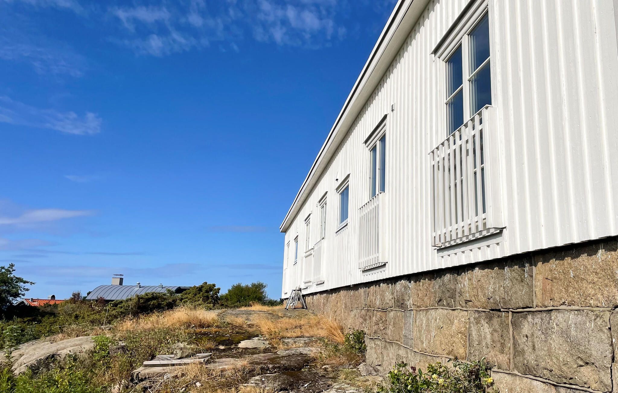 En vit byggnad med en grund av sten, en klarblå himmel och en liten båt på klippor.