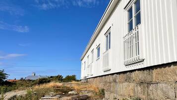 En vit byggnad med en grund av sten, en klarblå himmel och en liten båt på klippor.
