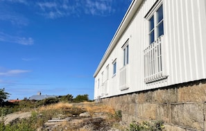 A white building with a stone foundation, a clear blue sky, and a small boat on rocks.