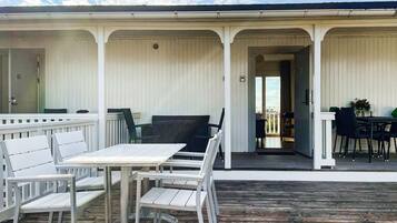 An outdoor seating area with white tables and chairs, a wooden deck, and a covered walkway with a view of the sky.