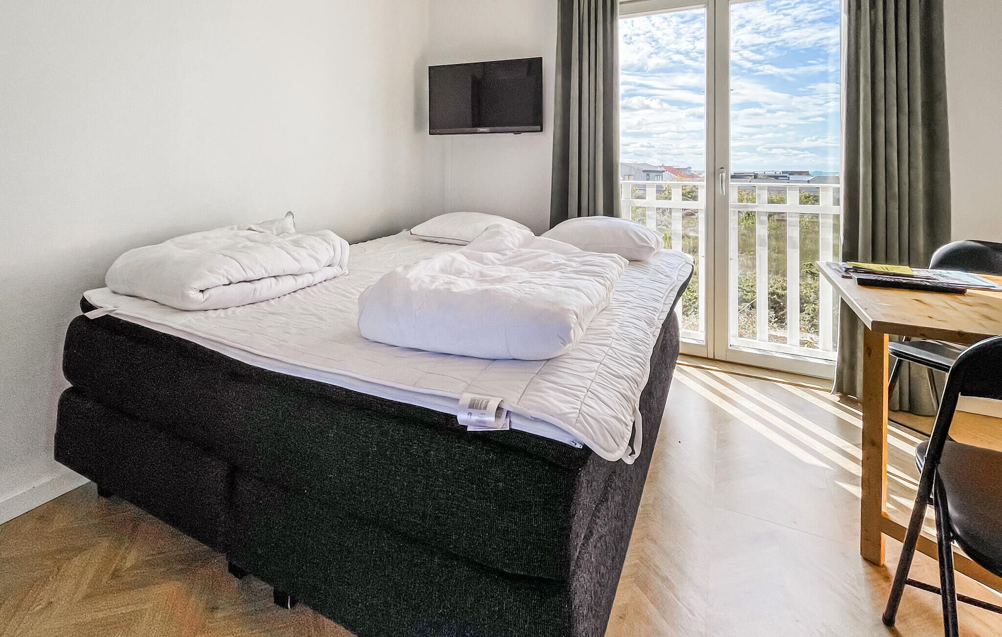 A hotel room with a bed, a desk, a chair, a television, and a balcony with a view.
