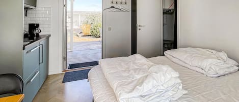 A hotel room with a bed, a desk with a coffee maker, a wardrobe, and a view of the outdoors.
