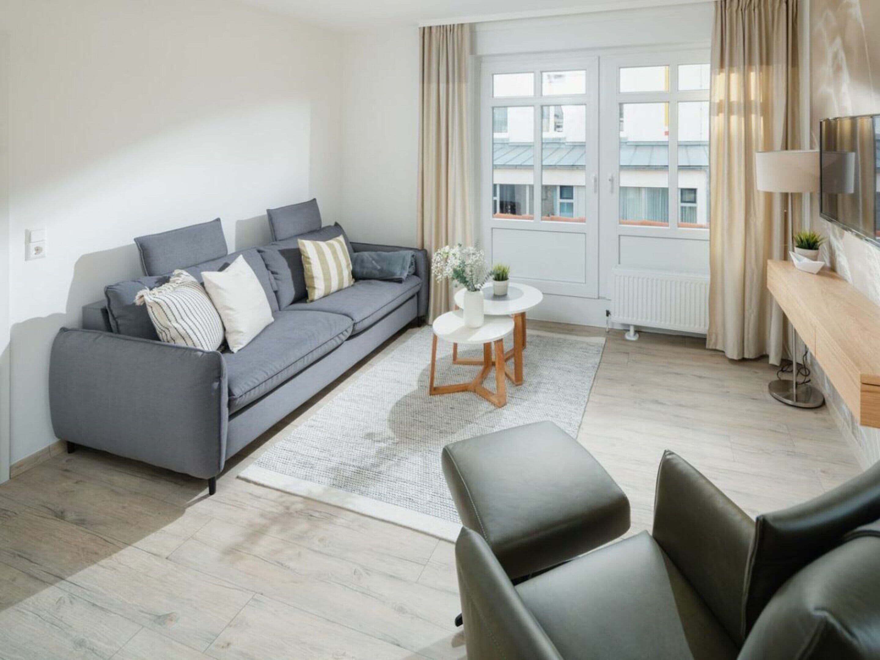 A modern living room with a grey sofa, a small round table, and a TV on a wooden stand.