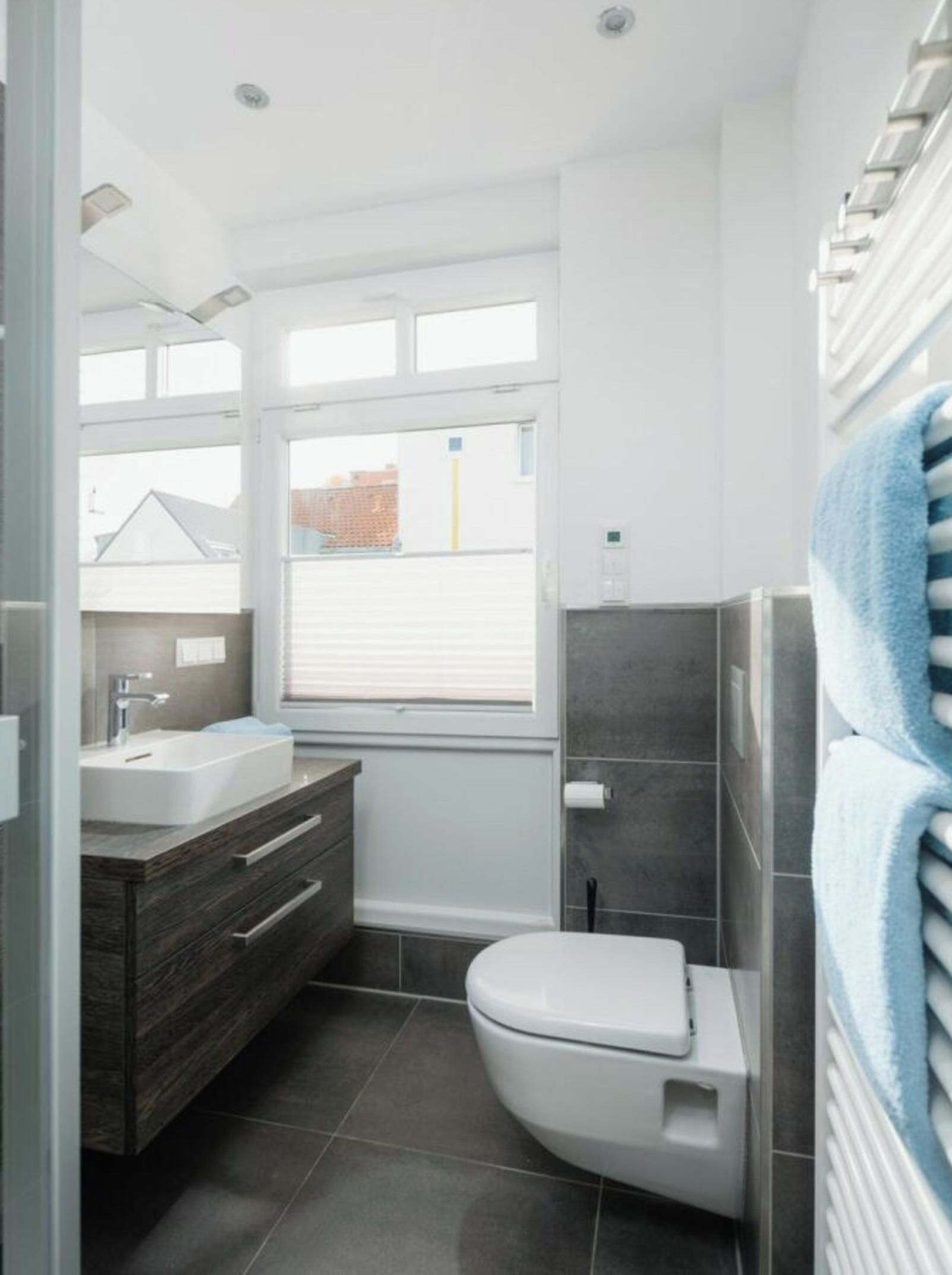 A modern bathroom with a white toilet, a sink, and a vanity. There is a window providing natural light and a view of the outside.