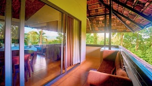 Un balcon doté d’une porte vitrée donnant sur un coin repas, un espace salon avec des sièges confortables et une vue sur la verdure.