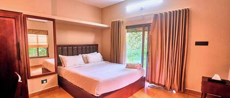 Quarto de hotel com uma cama grande, ventoinha no teto, janela com cortinas e mesa de cabeceira.
