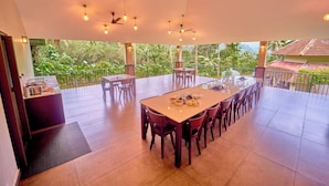 Une salle à manger spacieuse, dotée d’une longue table et de chaises, et entourée d’un balcon offrant une vue sur une végétation luxuriante.
