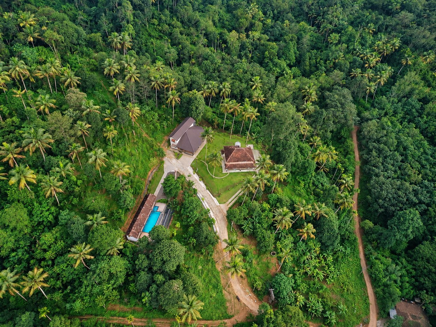 Vista aérea de una propiedad con piscina, una casa de huéspedes y un amplio jardín rodeado de densa vegetación tropical.