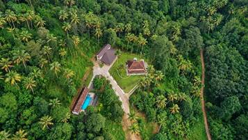 Vista aérea de una propiedad con piscina, una casa de huéspedes y un amplio jardín rodeado de densa vegetación tropical.
