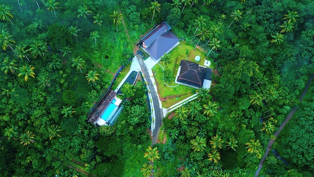 Vue aérienne d’un complexe hôtelier doté d’une piscine, d’une maison d’hôtes et d’un vaste jardin, le tout entouré d’une végétation tropicale luxuriante.