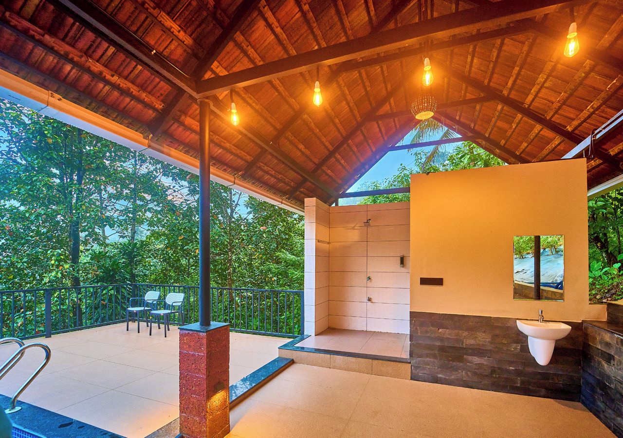 A covered outdoor area with a shower, seating, and a view of greenery.