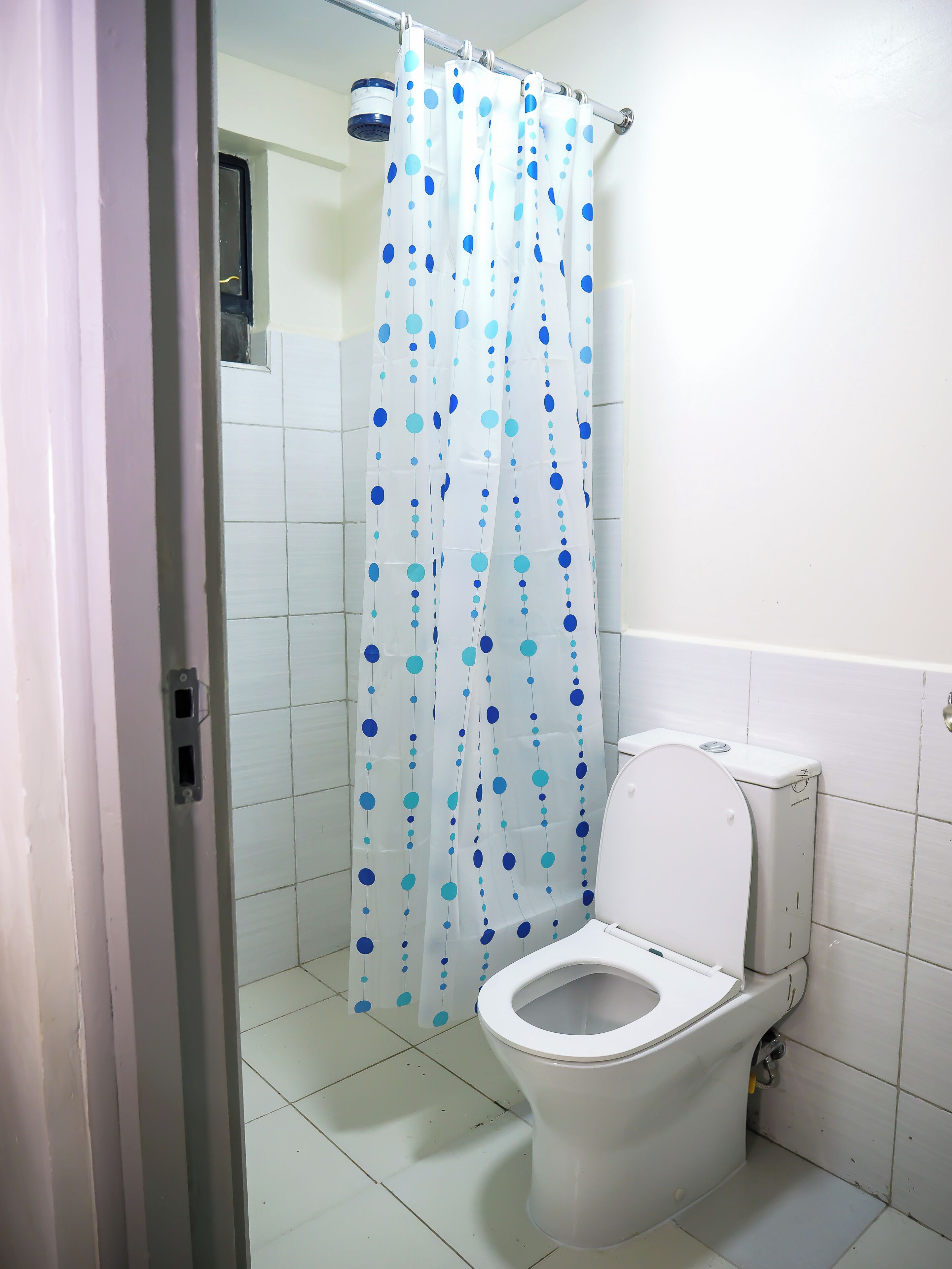 Une salle de bain avec des toilettes blanches, un rideau de douche à pois bleus et des murs carrelés.