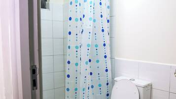 Une salle de bain avec des toilettes blanches, un rideau de douche à pois bleus et des murs carrelés.