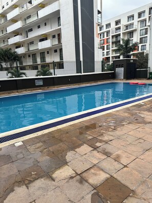A swimming pool with a tiled deck, surrounded by multi-story residential buildings. - Cozy studio apartment in a nice quiet space with a gym and pool (Nairobi)