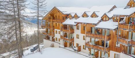 Un bâtiment en bois à plusieurs étages, doté de balcons, entouré d’un paysage enneigé et d’arbres.